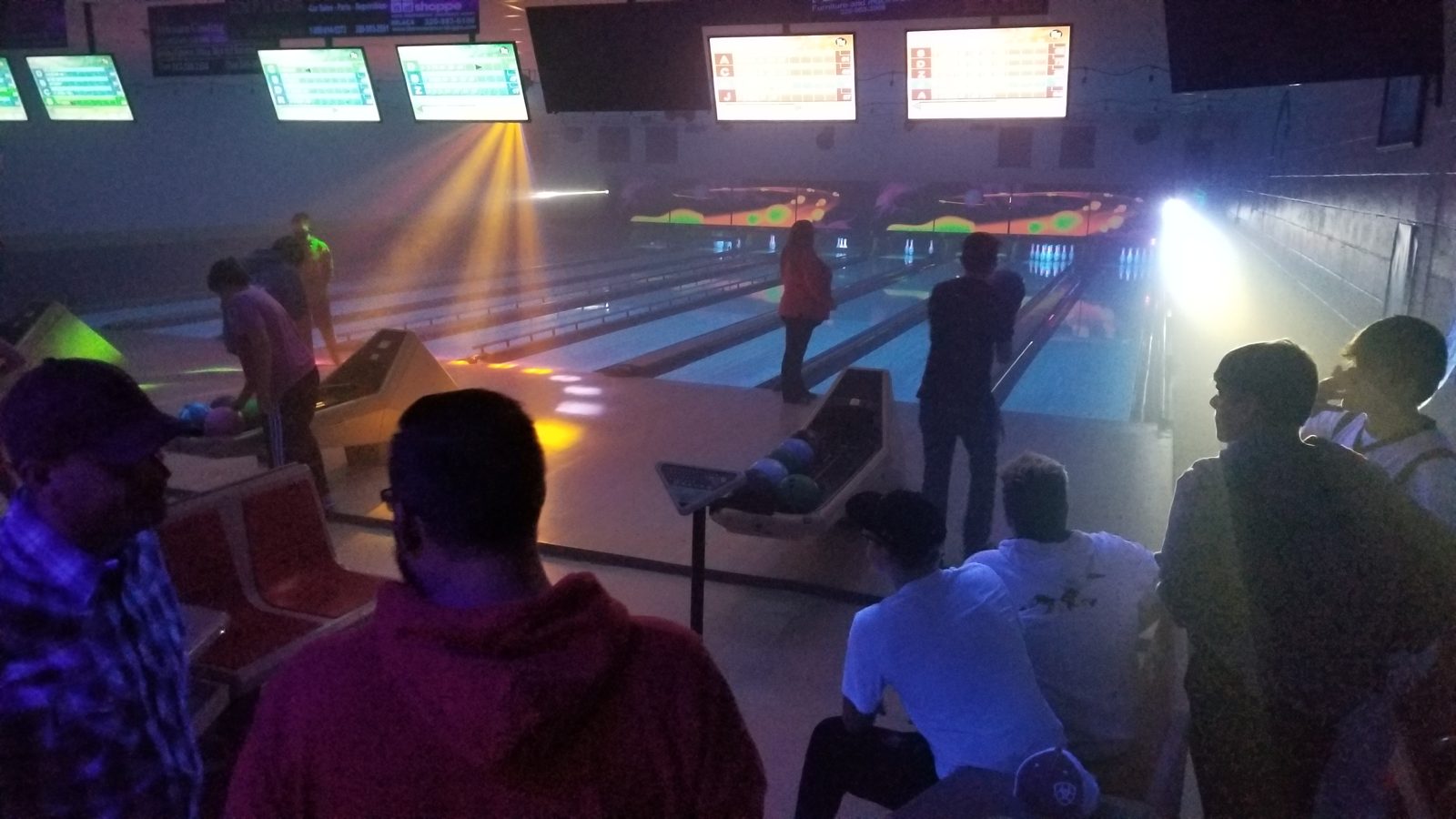 Bowlers on the lanes during Cosmic Bowling with light beams and fog